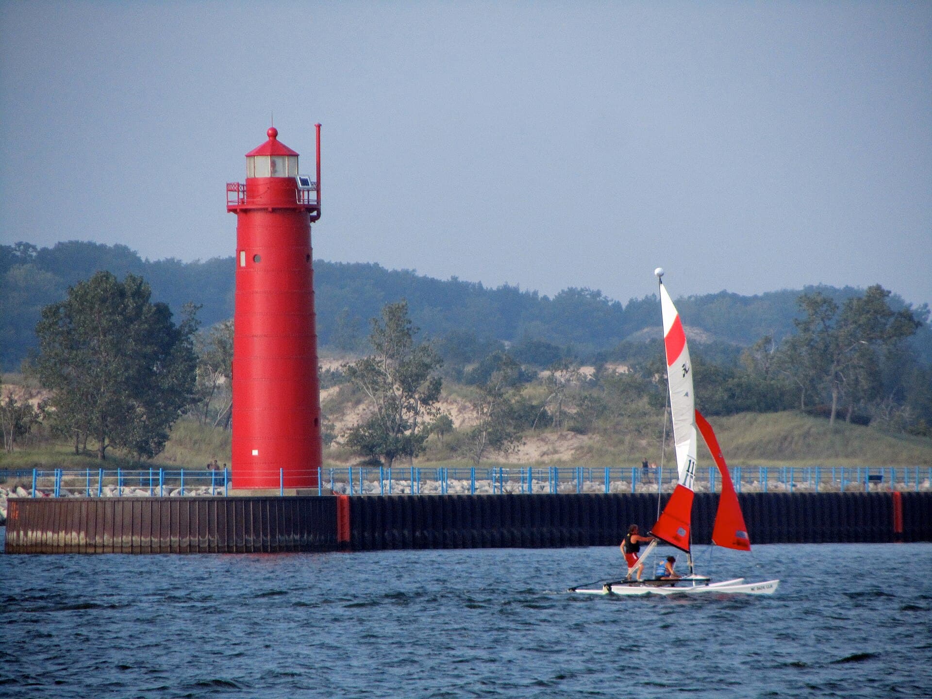 The red Muskegon pier lighthouse and a sailboat on a clear summer day at Pere Marquette Beach
