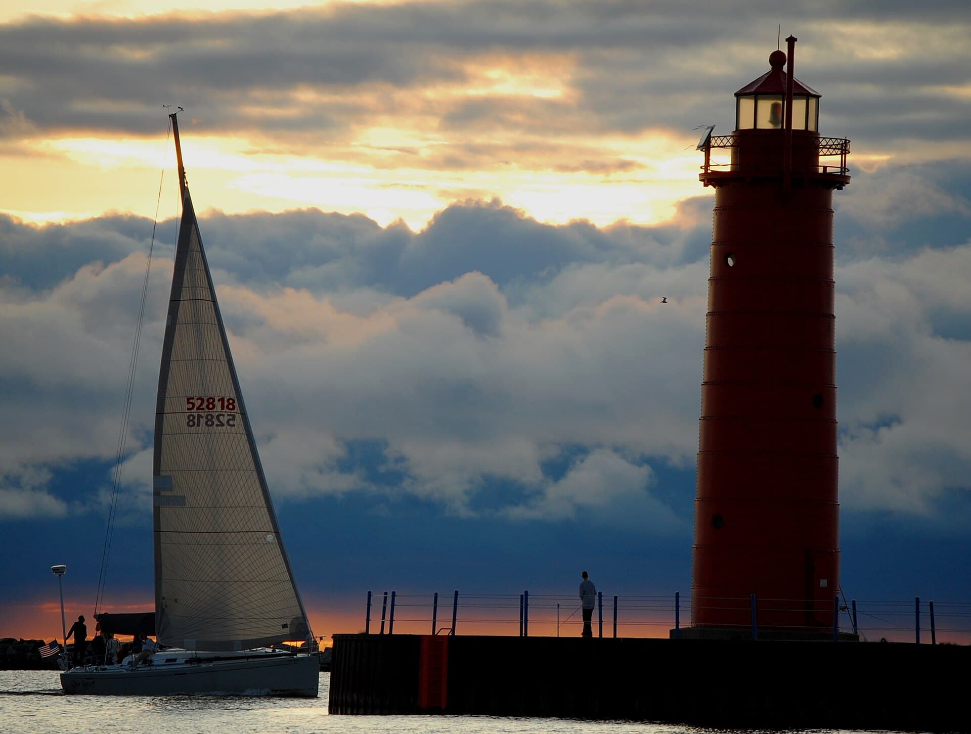 A sailboat passing the Muskegon South Pierhead Light at sunset off Pere Marquette Beach